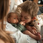 A heartwarming moment as a young child embraces a newborn sibling with mother nearby.