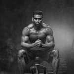 A powerful bodybuilder sitting with intense focus, showcasing muscular definition and strength.